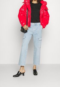 Chaqueta acolchada roja brillante, camiseta negra, vaqueros cargo azul claro con bolsillos y mules negras de tacón. Estilo casual urbano.