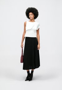 White, asymmetrical top with a ruffle detail, paired with a long, black, pleated skirt. Black ankle boots and a small, burgundy handbag.