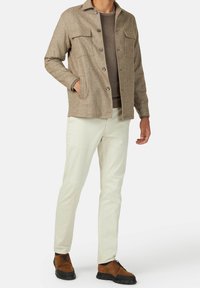 Brunprickig yllejacka med två bröstfickor, knäppning fram och en något texturerad yta. Matchas med ljusa byxor och bruna skor.