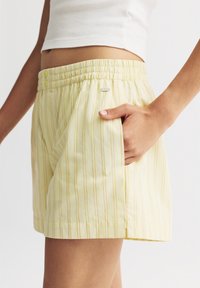 Gelbe gestreifte Shorts mit elastischem Bund, ausgestattet mit einer Seitentasche und einem kleinen Logotag. Hergestellt aus leichtem Stoff.