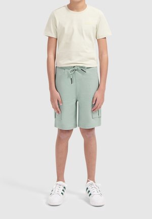 Lichtbeige t-shirt met een klein logo, gecombineerd met mintgroene cargo shorts met een trekkoord en twee zijzakken. Witte sneakers.