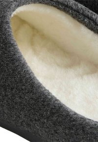 Zapatilla gris de felpa con un suave forro blanco, apertura redondeada y suela negra sólida. Superficie texturizada con un interior liso.