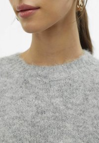 Grauer gestrickter Pullover mit rundem Ausschnitt, der eine weiche, flauschige Textur und ein dezentes Melange-Muster aufweist. Nahaufnahme des Ausschnitts und der Schulter.