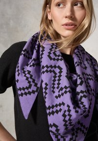 Sciarpa a fantasia viola e nera realizzata in morbido tessuto, drappeggiata liberamente attorno al collo, con una forma triangolare e dettagli a zigzag.