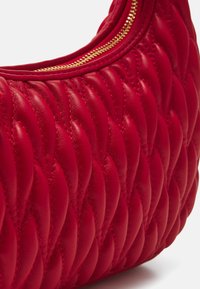 Sac à main en cuir rouge avec un design matelassé, une surface texturée et une fermeture éclair dorée sur le dessus.