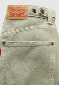 Jean en denim vert clair Levi's montrant la poche arrière, les rivets, le patch en cuir de la marque et la fermeture par bouton.