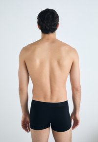 Schwarze Boxershorts aus glattem Stoff, die ein figurbetontes Design und einen elastischen Bund aufweisen. Das Modell ist von hinten zu sehen, ohne Oberbekleidung.