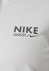 Hvidt stof med sort Nike-logo og swoosh trykt på, med diagonale stribedesign under teksten.
