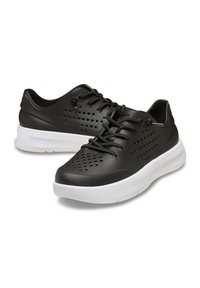 Zapatillas deportivas negras hechas de un material texturizado, con perforaciones para transpirabilidad, cordones negros y una suela blanca acolchada.