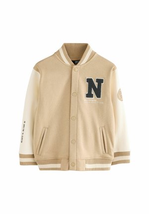 Veste varsity beige avec manches crème, col, poignets et bas rayés en côtes, patch noir "N" sur la poitrine et coordonnées imprimées sur la manche.