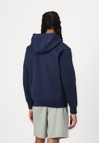 Sweatshirt azul-marinho com capuz, ajuste relaxado, material misto de algodão, punhos e barra canelados, mostrada de costas com textura suave.