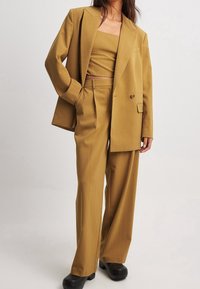 Traje de dos piezas beige que incluye una chaqueta de doble botonadura con cuello de muesca, pantalones de pierna ancha y una parte superior corta con una textura suave.
