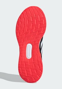 Semelle de chaussure avec un fond en caoutchouc texturé rouge présentant un motif de bande de roulement surélevé ; accents noir et blanc le long des côtés.