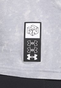 Šedá bavlněná tkanina s jemnou strukturou; obsahuje černou etiketu se značkou Under Armour a názvem značky v bílé barvě.