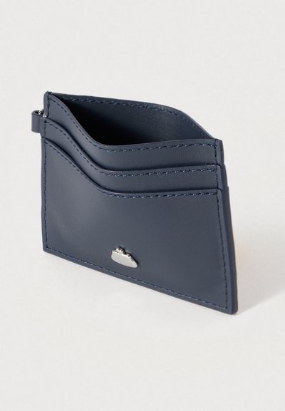 Δερμάτινο θήκη καρτών σε ναυτικό μπλε με τρεις θήκες για κάρτες και ασημένια λεπτομέρεια στο κάτω μέρος. Διαθέτει καθαρές ραφές και λεία υφή.
