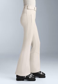 Jasno beżowe spodnie w fasonie dzwonów z widocznymi szwami. Wysoki stan z paskowymi pętelkami. Połączone z czarnymi butami z srebrnymi akcentami.