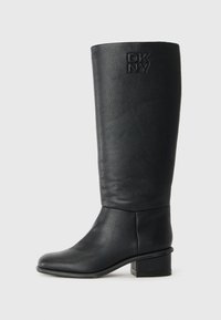 Bota de couro preta até ao joelho com um acabamento texturizado, bico arredondado e um tacão baixo em bloco. Apresenta o logotipo em relevo da DKNY no lado externo do cano.
