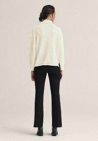 Kermansävyinen neulepaita, jossa korkea kaulus, resorireunus ja sivuhalkiot, yhdistetty mustiin istuviin housuihin ja lohkokoroisiin saappaisiin. Rakennekangas.