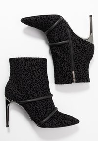 Bottines à talons noirs en tissu texturé avec un motif léopard. Dotées d'une fermeture éclair et de deux bandes noires en accent.
