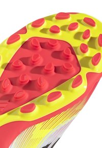 Punaiset ja keltaiset nappulakengät, joissa on useita kapenevia piikkejä, kiiltävä pinta ja teksturoitu pinta, jossa on vinosti valkoisia viivoja.