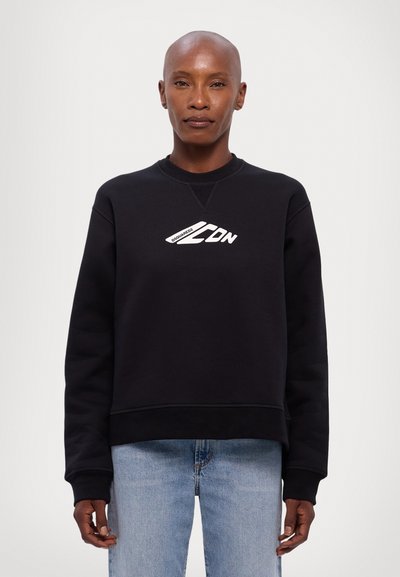 Sort sweatshirt med rund hals, ribbede manchetter og kant, der har hvid grafisk tekst foran. Bæres med lyseblå jeans.