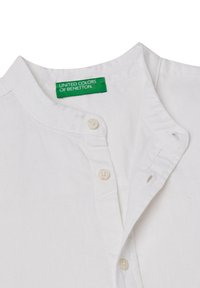 Camicia bianca con colletto rialzato, abbottonatura e logo ricamato. Realizzata in tessuto leggero, presenta una consistenza morbida e bottoni color crema.