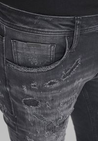 Vaqueros de mezclilla negros con detalles desgastados y parches deshilachados. Cuenta con un bolsillo trasero con una etiqueta de marca. Tela texturizada, ajuste tapered.