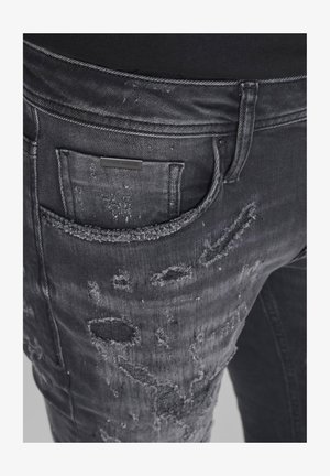 Jeans in denim nero con dettagli strappati e toppe sfrangiate. Presentano una tasca posteriore con etichetta del marchio. Tessuto consistenza, vestibilità aderente.