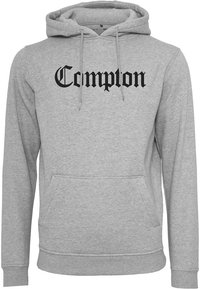 Šedá bavlněná mikina s kapucí, která má přední kapsu a černý nápis "Compton" v tučném, dekorativním písmu.