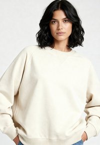 Sweat-shirt couleur crème à coupe décontractée, poignets côtelés et col rond. Texture douce et design minimaliste avec une légère couture en V au niveau de l'encolure.