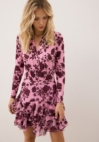 Bloemeneis met een roze basis en donkere rode rozenpatronen, lange mouwen, een v-halslijn en een gelaagde rucheszoom.