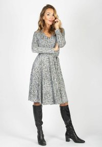 Szara sukienka w wzory z długimi rękawami i dekoltem w serek, taliowana, sięgająca do połowy łydki. Noszona z czarnymi, wysokimi do kolan kozakami.