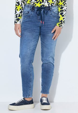 Person iført blå snørelommer jeans, sorte og hvide sneakers med tykke såler og en farverig langærmet skjorte med gule stjernemønstre.