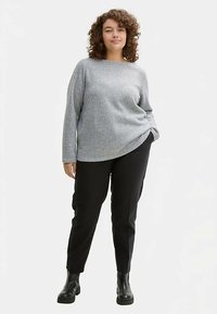 Grijze wollen trui met een ontspannen pasvorm, lange mouwen en een ronde halslijn, gecombineerd met zwarte broek en enkellaarsjes.