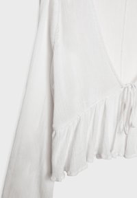Weiße Bluse aus leichtem, strukturiertem Stoff mit einem Rüschensaum, V-Ausschnitt und Bindeschluss. Das Design verfügt über lange Ärmel mit einem lockeren Schnitt.