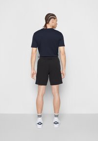 Shorts sportivi neri con cintura elasticizzata, abbinati a una maglietta nera. Indossati con sneakers bianche con dettagli neri.