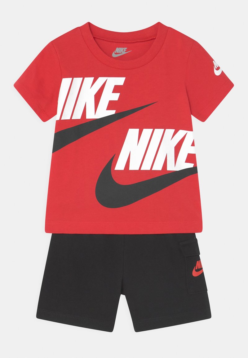 Crvena pamučna majica s bijelim i crnim Nike logotipom, upotrebljena u kombinaciji s crnim šortsem koji ima bočnu džep i mali crveni Nike logotip.