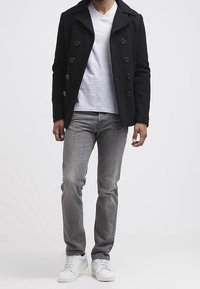 Black peacoat with double-breasted button closure, gray V-neck shirt, gray jeans, and white sneakers. Smooth texture, tailored fit.
