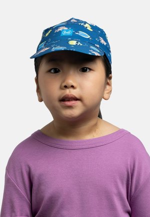 Niño con una gorra azul con patrones de peces coloridos y una camisa morada, mirando ligeramente hacia arriba sobre un fondo liso.