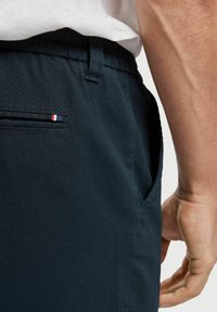 Tmavě námořnicky modré šortky z texturované látky, s boční kapsou a malým tříbarevným detailem u zadní kapsy, elastický pas.