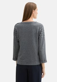 Top grigio e blu a quadri con maniche a tre quarti, scollatura rotonda e vestibilità ampia. Tessuto testurizzato con un motivo a griglia.