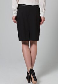 Jupe crayon noire ajustée avec une fente à l'arrière, en tissu lisse et avec un minimum de détails, associée à des chaussures à talons hauts noires.