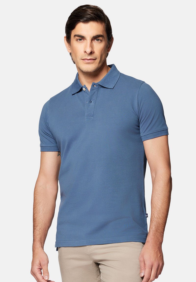 Niebieska koszulka polo z krótkim rękawem, z kołnierzykiem, dwoma guzikami, klasycznym krojem i gładką teksturą, zestawiona z beżowymi spodniami.