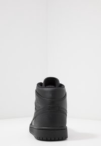 Czarny, wysoki sneakers z tyłu, umieszczony na białej powierzchni z gładkim, białym tłem.