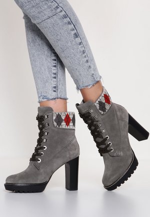 Bottines en suède gris avec un revers à carreaux texturé en rouge, gris et noir. Dotées d'un talon épais et d'une semelle en caoutchouc avec un motif de nervures visible.