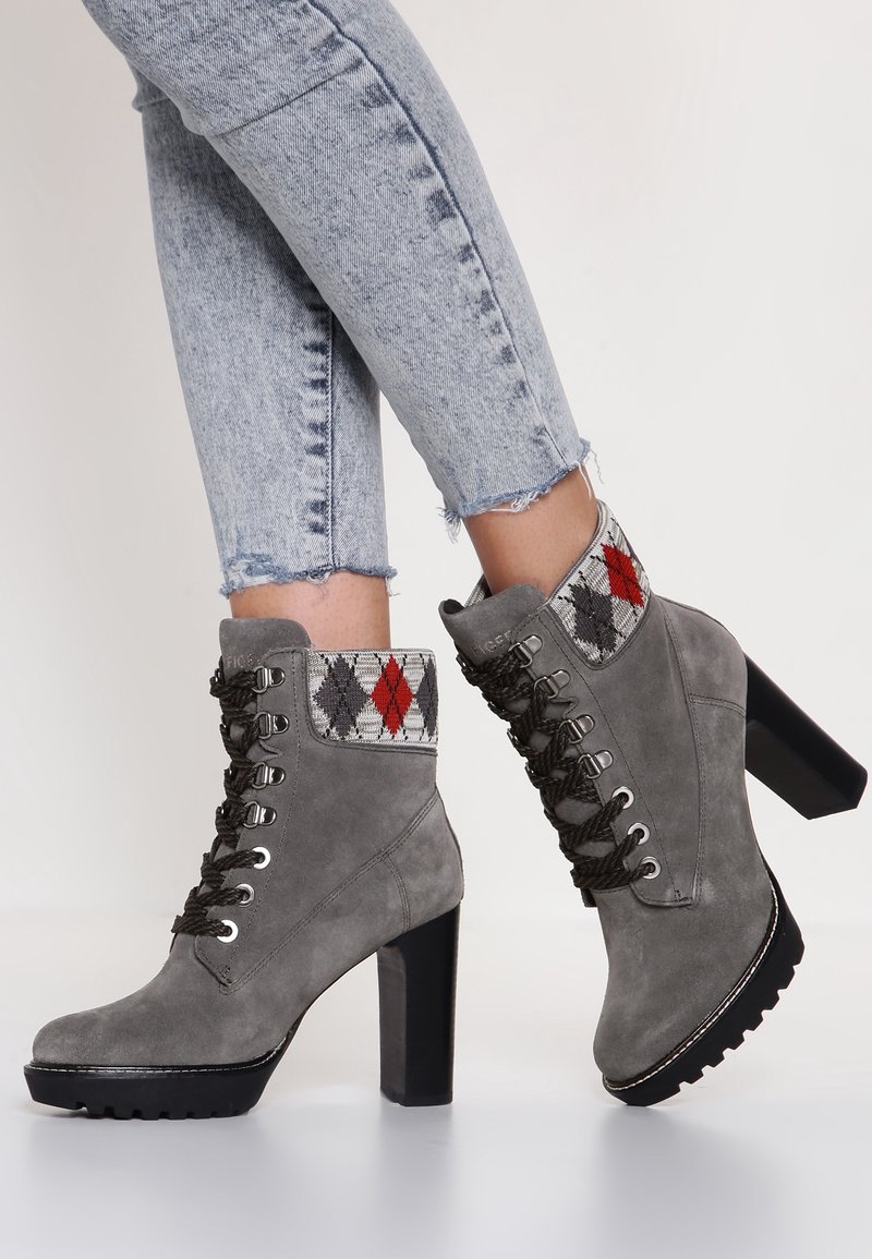 Bottines en suède gris avec un revers à carreaux texturé en rouge, gris et noir. Dotées d'un talon épais et d'une semelle en caoutchouc avec un motif de nervures visible.