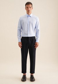 Jasnoniebieska koszula z guzikami, czarne spodnie plisowane i czarne buty eleganckie. Koszula ma klasyczny kołnierzyk i długie rękawy.
