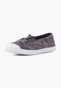 Zapatilla slip-on de lona gris con suela de goma blanca, con tres ojales plateados, textura suave y puntera redondeada con tapa texturizada.