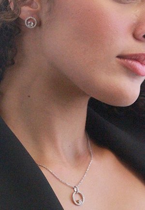 Collana in argento con pendente circolare che presenta una piccola pietra centrale, abbinata a orecchini a bottone rotondi coordinati, entrambi decorati con piccoli cristalli.