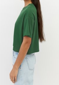 Maglietta verde a maniche corte in tessuto morbido, accoppiata con jeans in denim azzurro chiaro a vita alta. Design semplice, senza fantasie.
